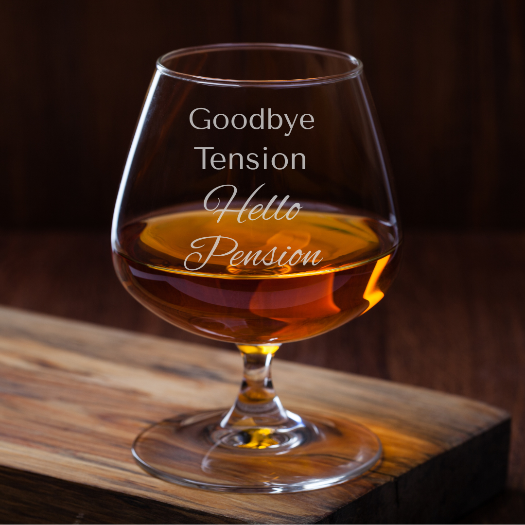 Glass of amber liquid with 'Goodbye Tension Hello Pension' text on a wooden surface.