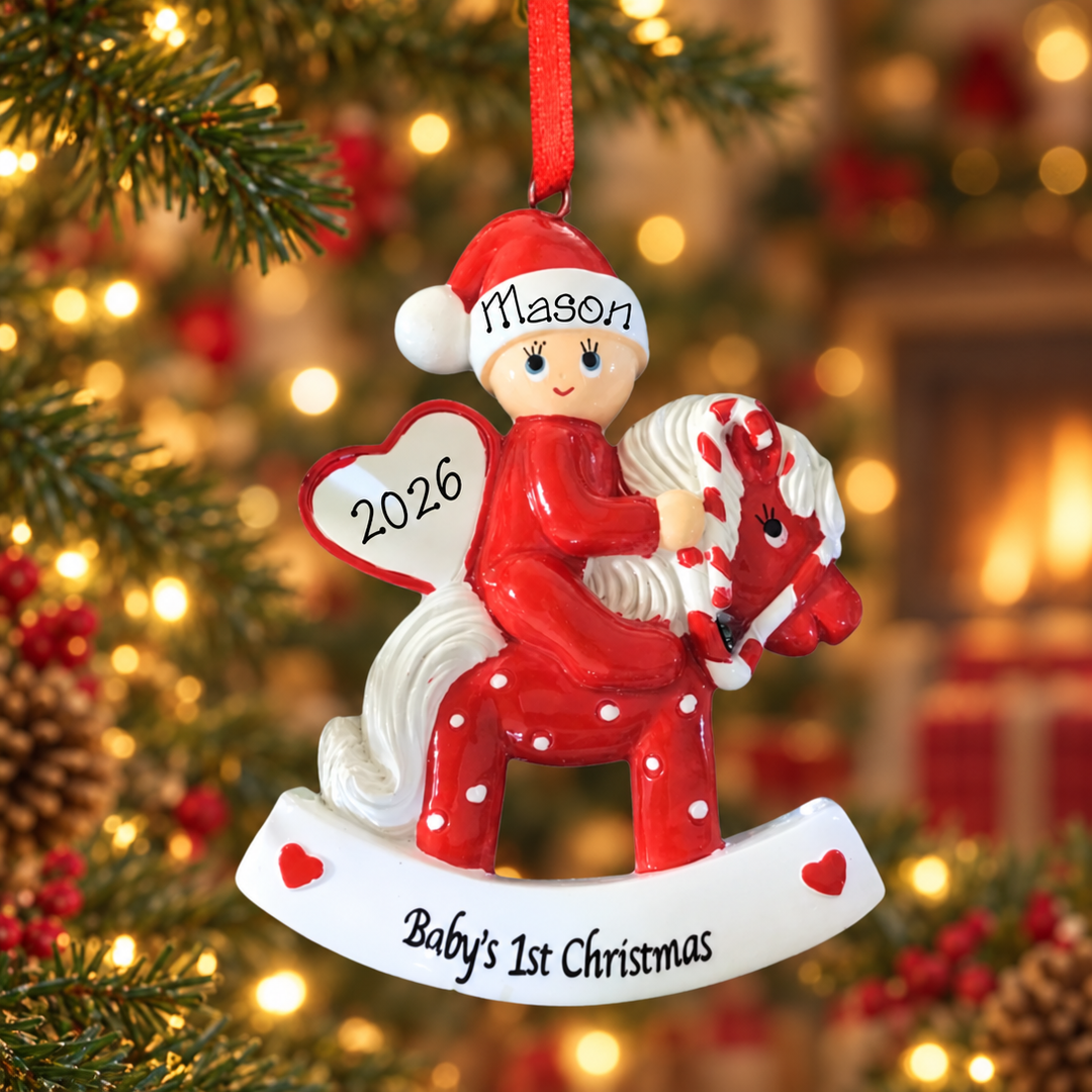 Personalized Christmas rocking horse ornament featuring a baby riding a red and white horse, hanging on a Christmas tree with warm holiday lights in the background. The ornament is customized with the name 'Mason' on the Santa hat, '2026' on the heart, and 'Baby's 1st Christmas' on the base.