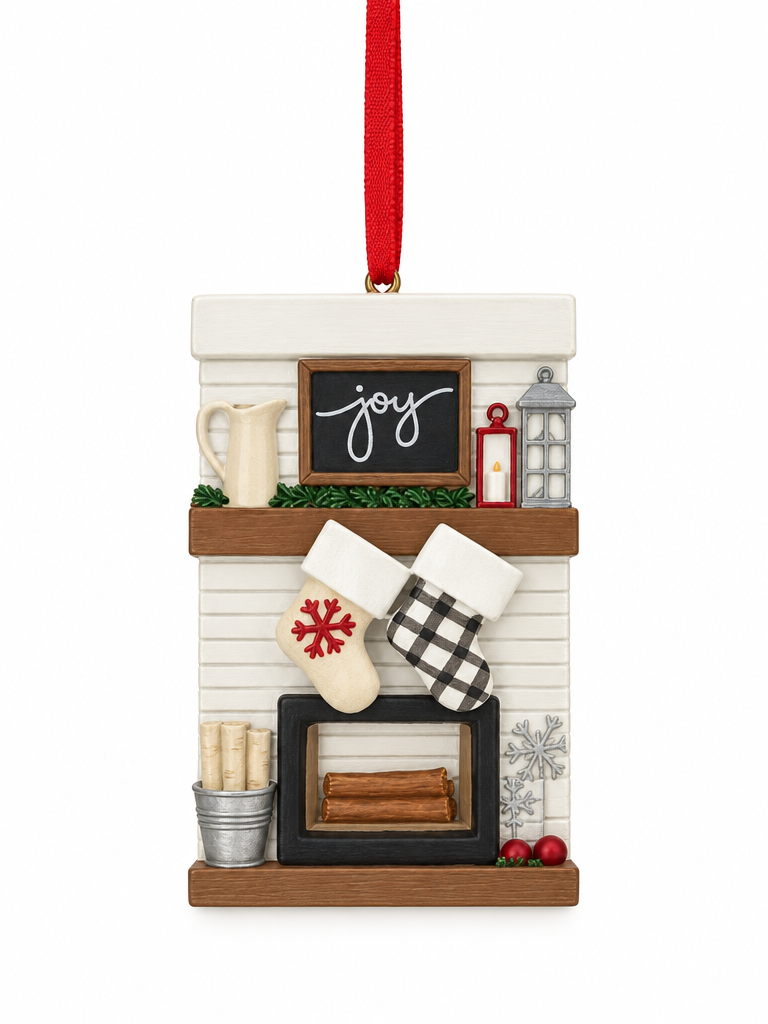 A Christmas ornament shaped like a fireplace mantel with a red hanging ribbon, white siding, brown wood shelves, a small chalkboard sign reading 'joy', stockings, a lantern, snowflake decorations, and red berries, shown on a white background.