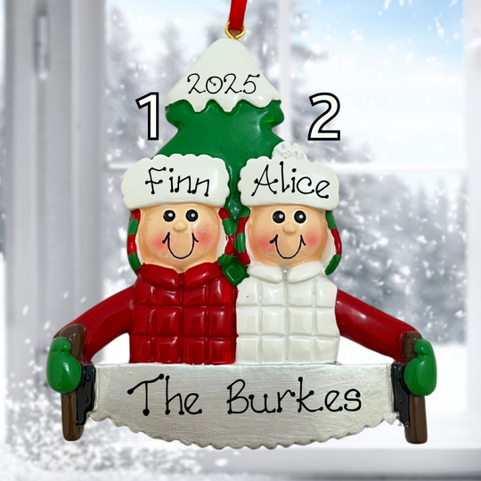 Personalized Christmas ornament with two children's names and a family name, set against a snowy window background.