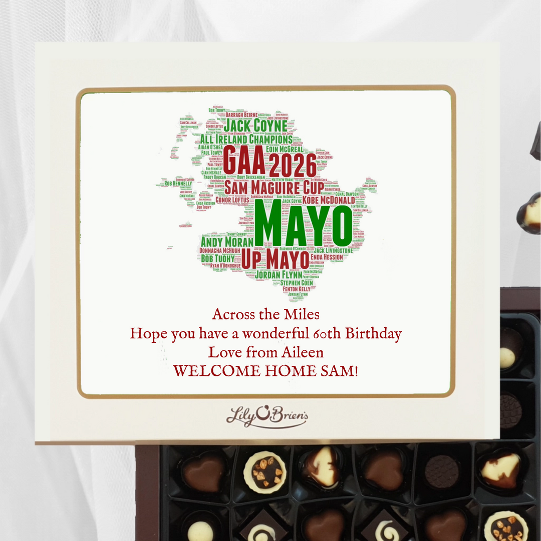 A personalized chocolate gift box from Lily O' Browns, featuring a cream-colored lid with a gold border and a word cloud shaped like the map of County Mayo. The text on the lid celebrates GAA 2026 Mayo and includes a warm homecoming message.