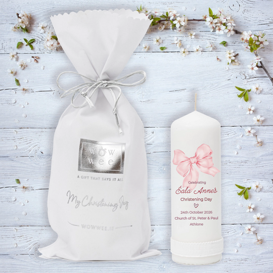 White gift bag and candle with floral decorations on a light wooden background