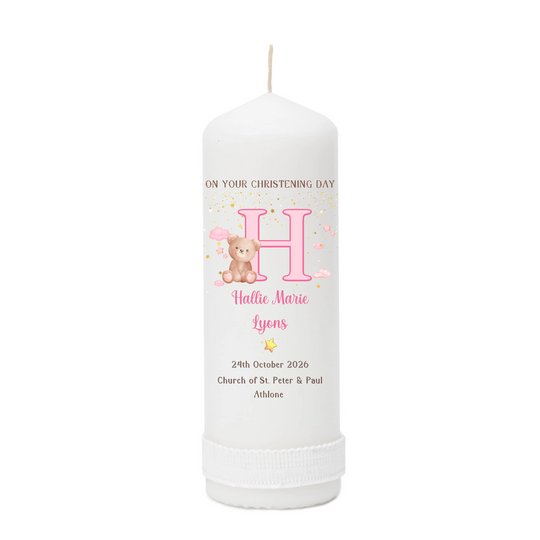 A personalized white pillar candle with a printed christening design featuring a large pink letter H.