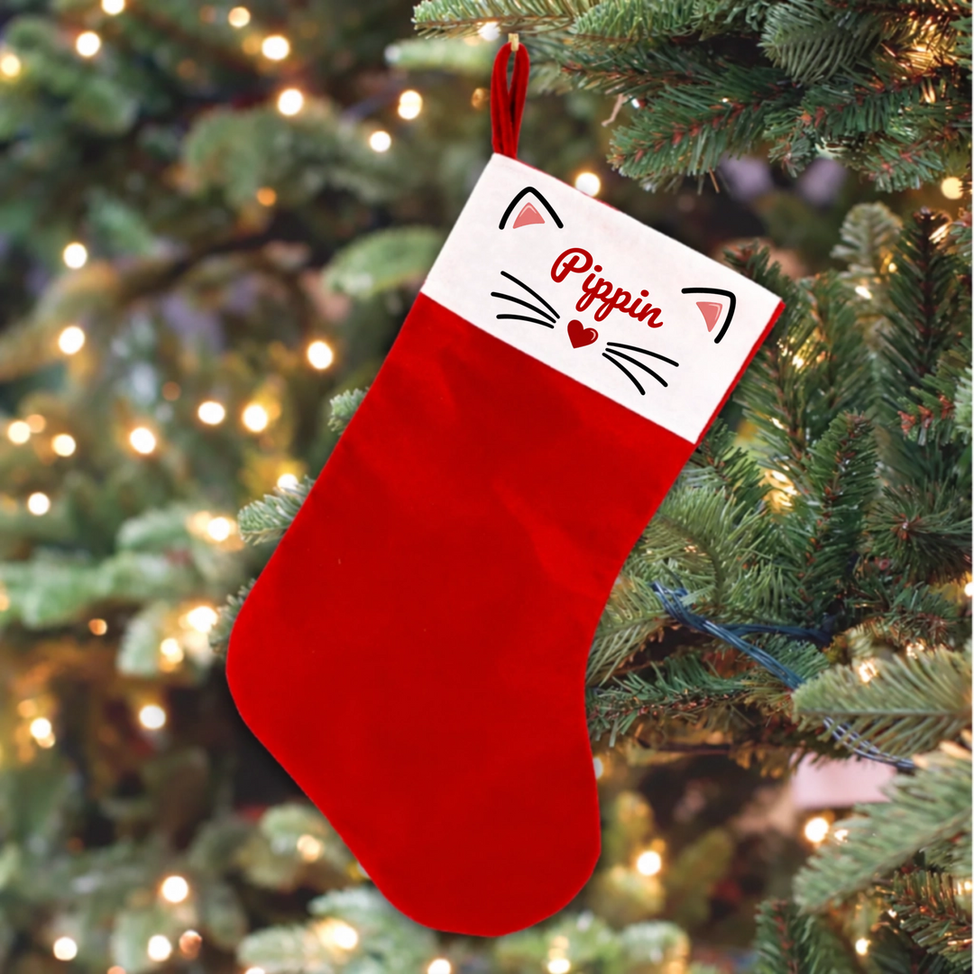 A red Christmas stocking hanging from a decorated Christmas tree. The stocking has a white cuff with the name 'Pippin' written in red script, along with small paw prints and heart illustrations.