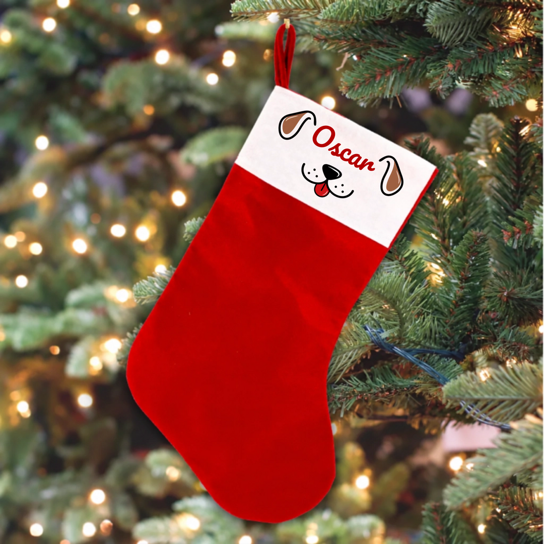 A red Christmas stocking hanging from a decorated Christmas tree. The stocking has a white cuff with the name 'Oscar' written in red script, along with small paw prints and heart illustrations.