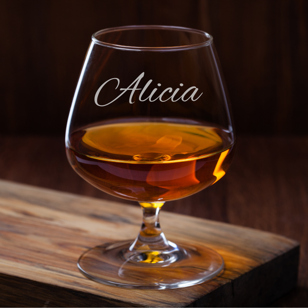 Glass of amber liquid with 'Alicia' engraving on a wooden surface