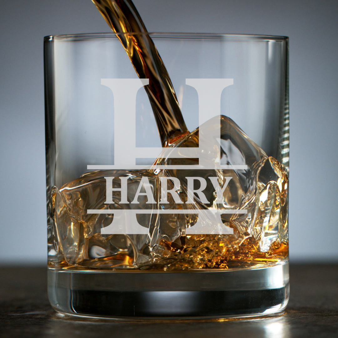 Glass of whiskey being poured with 'HARRY' engraved on it, against a gray background