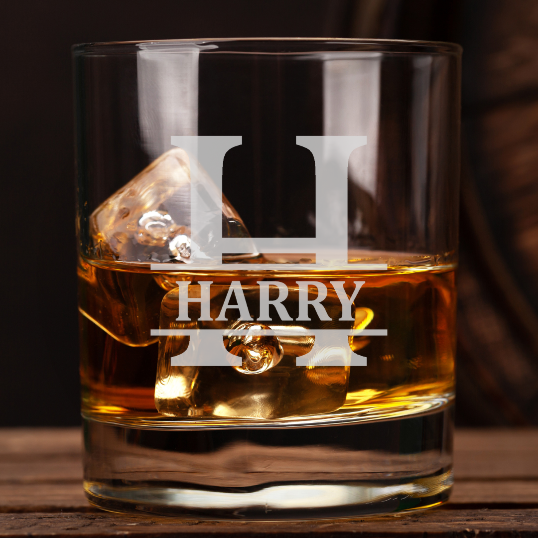 Glass of whiskey with ice cubes and 'HARRY' engraving on a wooden surface