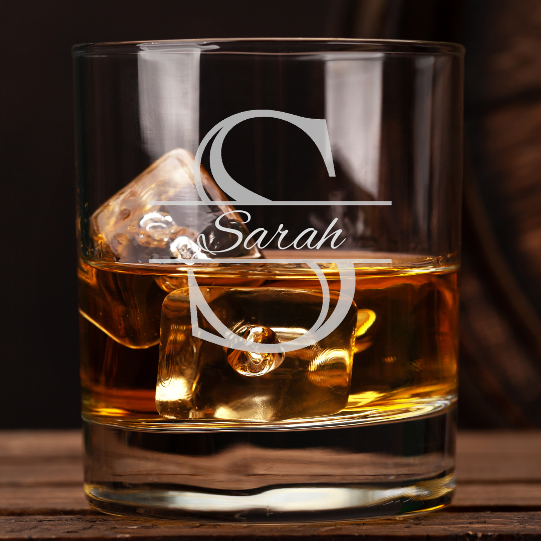 Glass of whiskey with ice cubes and 'Sarah' monogram on a wooden surface
