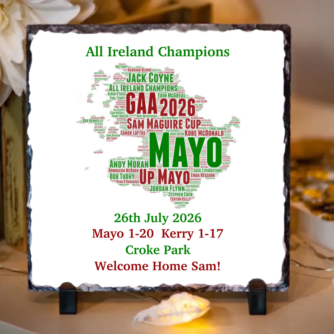 A square slate sign on a small black stand, featuring a white background with a map of Ireland filled with green and red text celebrating GAA winners and match results. The sign reads 'All Ireland Champions' and 'GAA 2026 SAM MAGUIRE CUP MAYO UP MAYO 26th July 2026 Mayo 1-20 Kerry 1-17 Croke Park Welcome Home Sam!'.