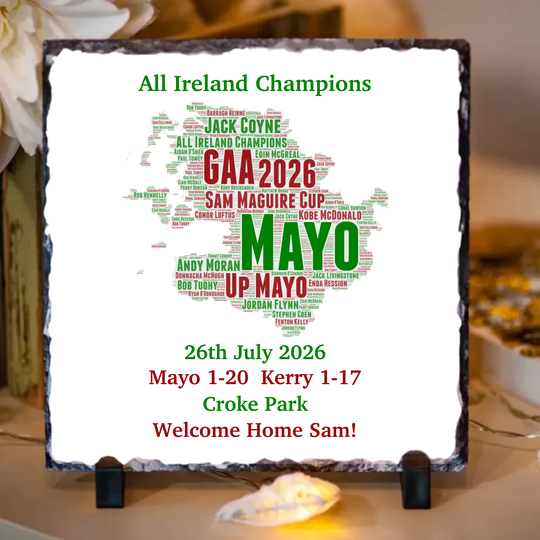 A square slate sign on a small black stand, featuring a white background with a map of Ireland filled with green and red text celebrating GAA winners and match results. The sign reads 'All Ireland Champions' and 'GAA 2026 SAM MAGUIRE CUP MAYO UP MAYO 26th July 2026 Mayo 1-20 Kerry 1-17 Croke Park Welcome Home Sam!'.