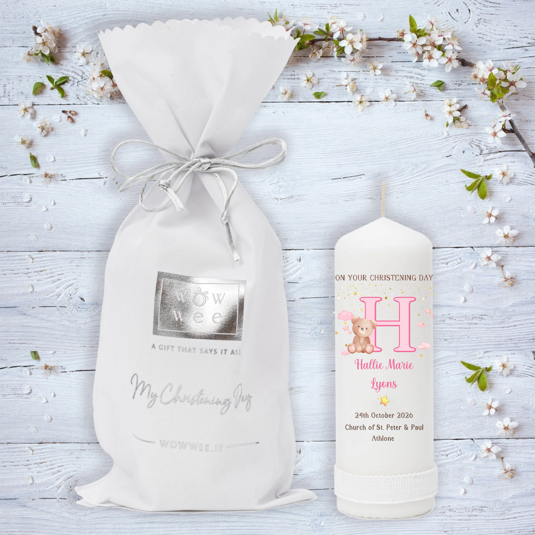 A personalized Christening gift set featuring a white drawstring pouch with a silver foil logo and a matching white candle. 