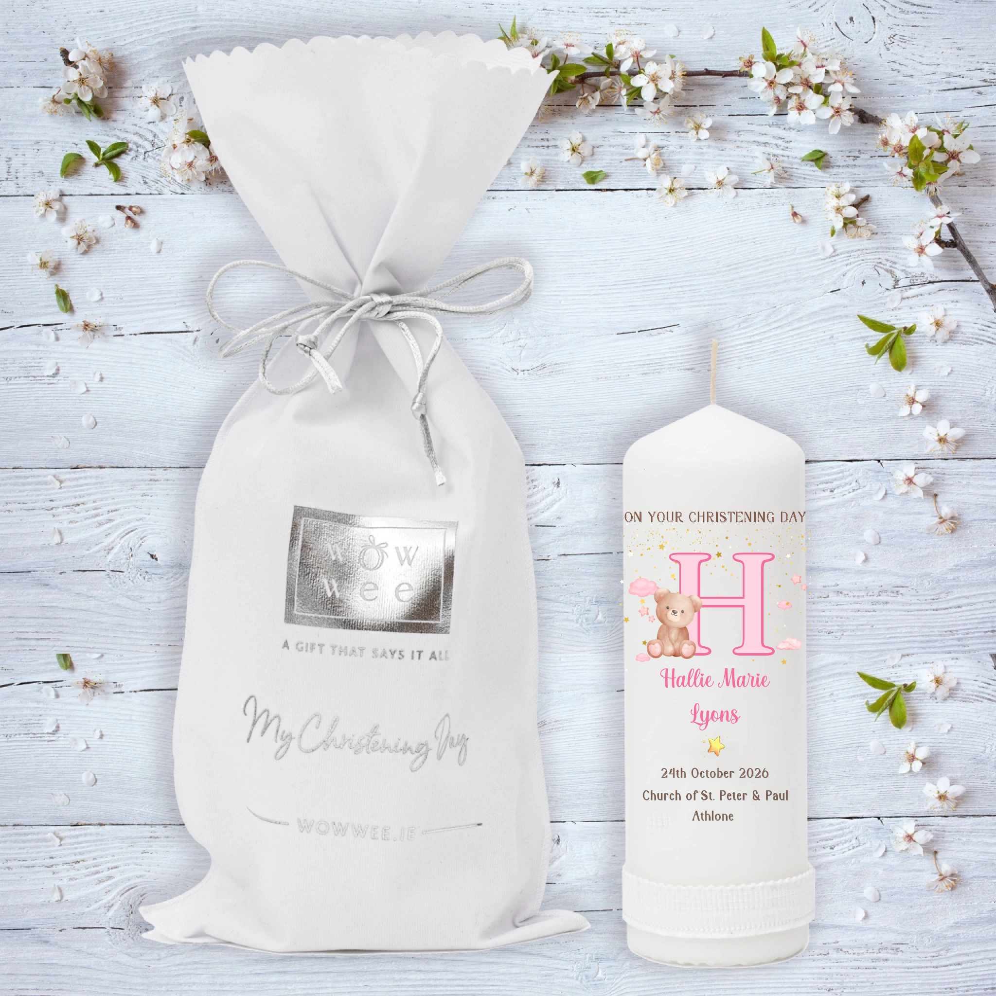 A personalized Christening gift set featuring a white drawstring pouch with a silver foil logo and a matching white candle. 