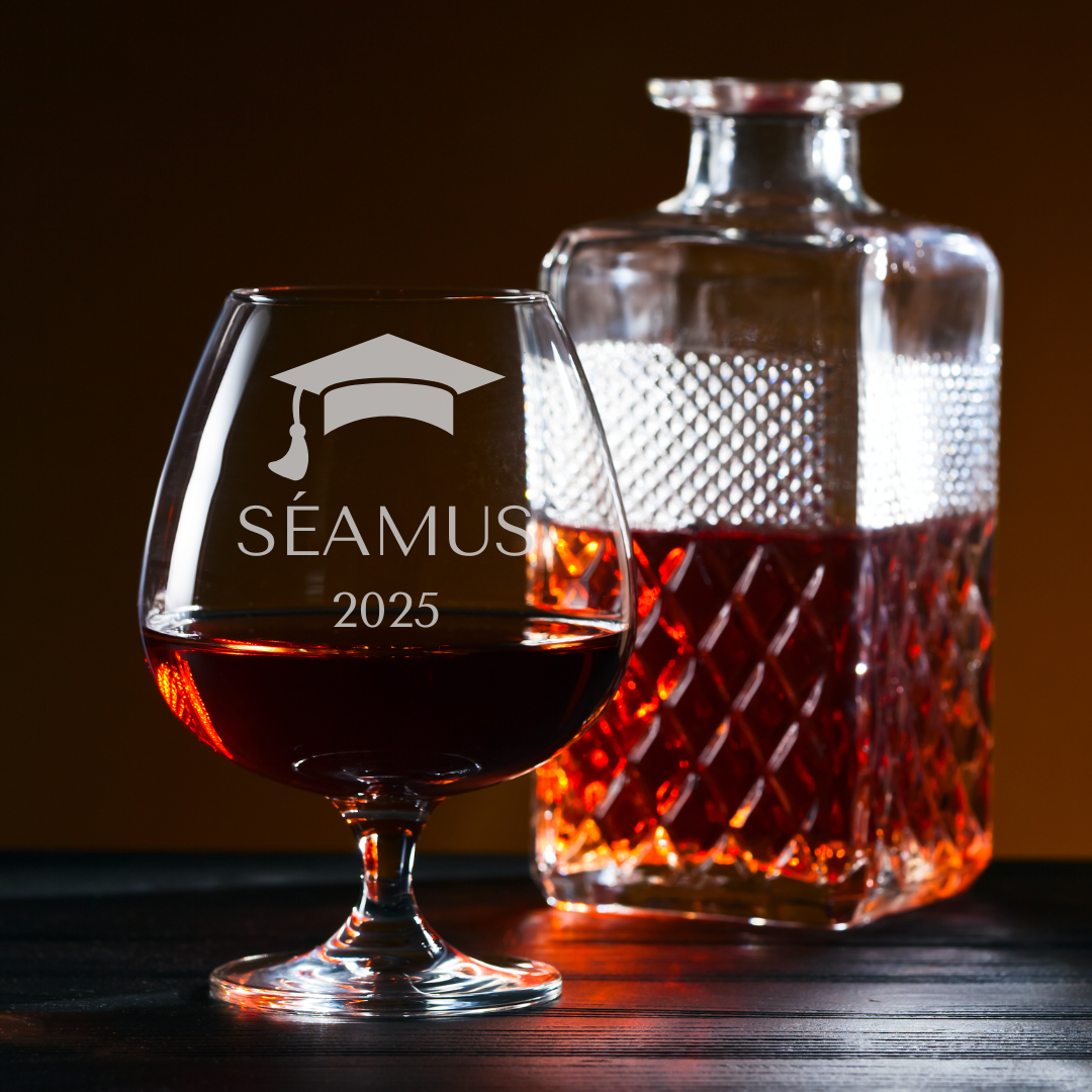 Snifter glass with 'Seamus 2025' engraving and a decanter filled with liquid on a dark background