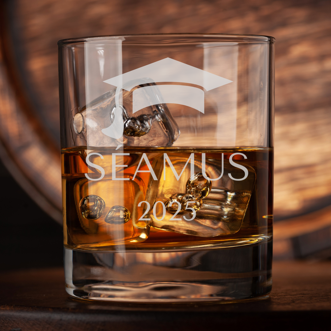 Glass of whiskey with ice cubes and 'SEAMUS 2025' engraving on a wooden surface.