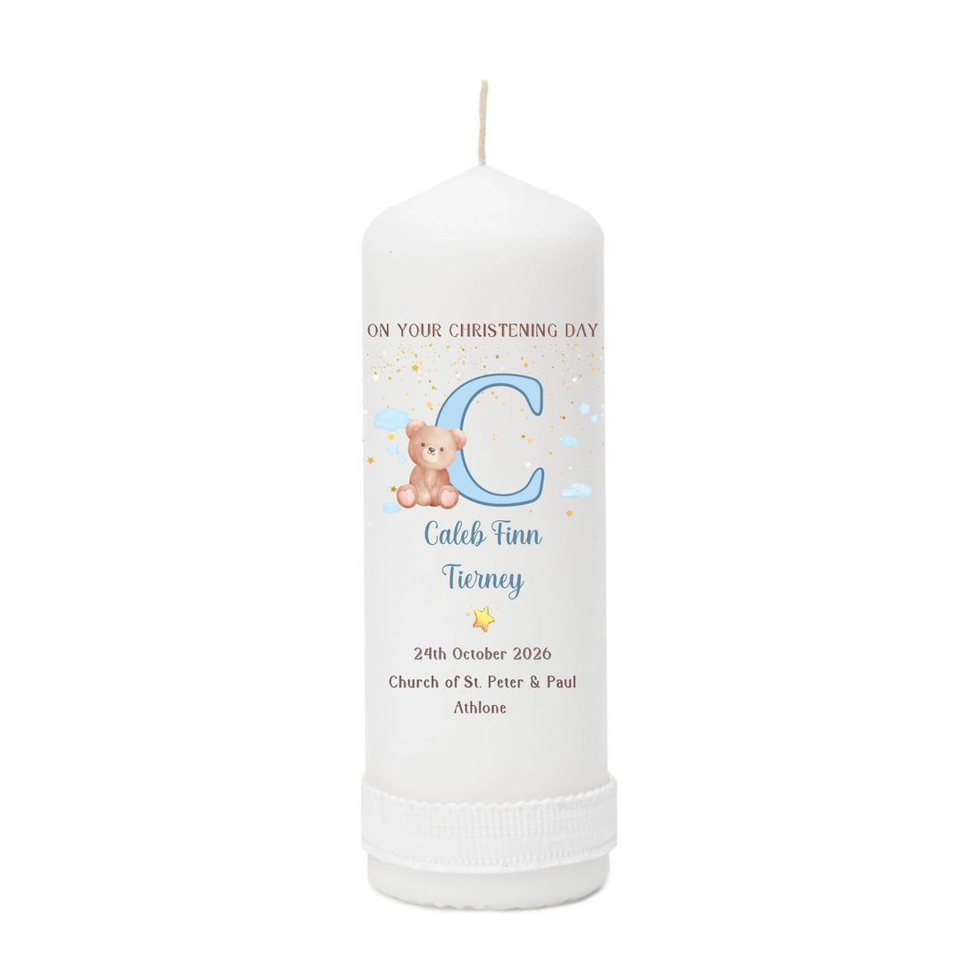 A personalized white pillar candle with a christening design, featuring a large blue letter 'C', a teddy bear, and custom text for a child named Caleb Finn Tierney, shown on a plain white background.