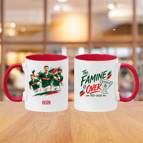 Two white ceramic mugs with red interiors and handles sit on a wooden table in a blurred indoor setting. The left mug shows a printed graphic of football players and the name OISIN below.