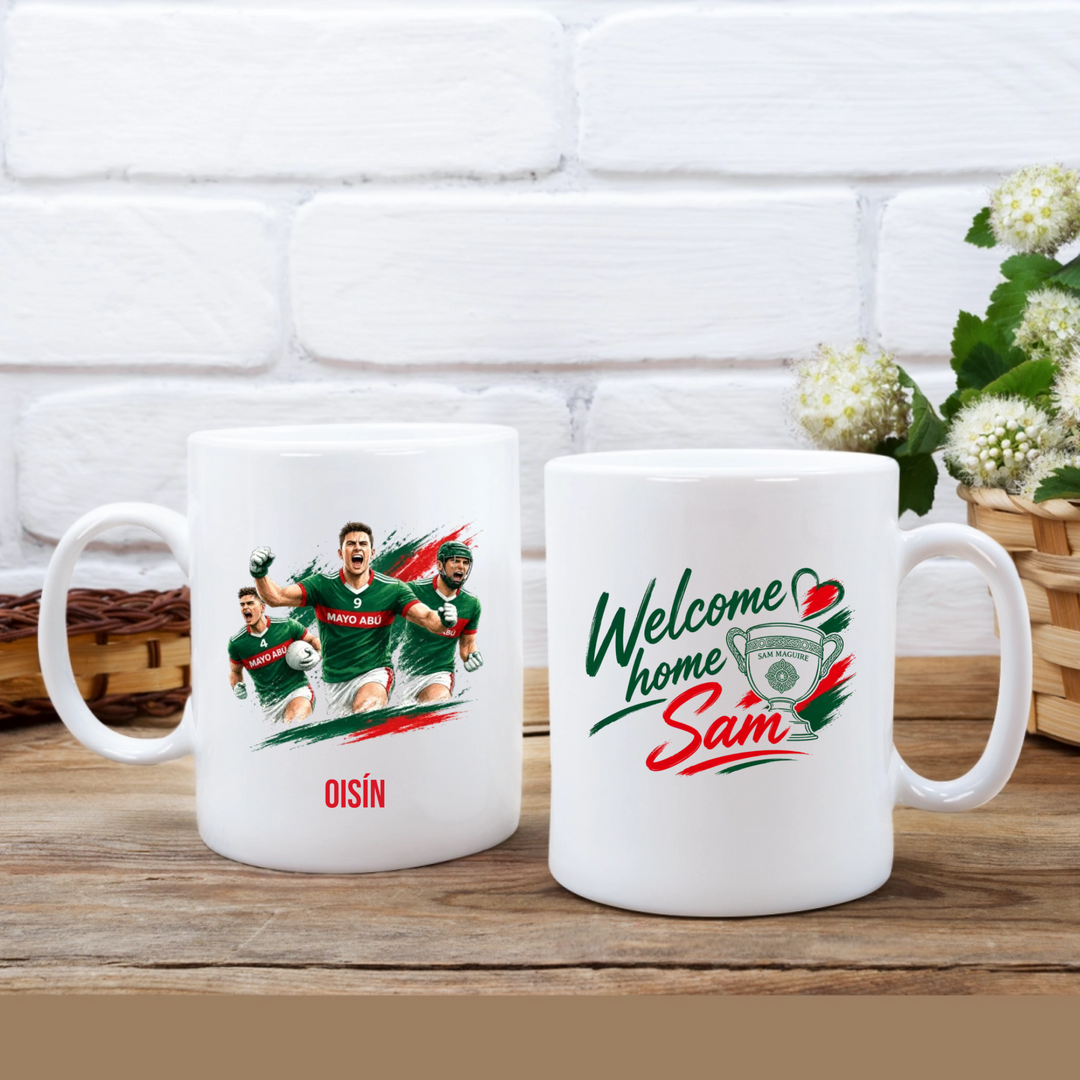 Two white ceramic mugs displayed side by side on a wooden table against a white brick wall. The left mug features a graphic of rugby players in green jerseys with the name 'OISÍN' below.