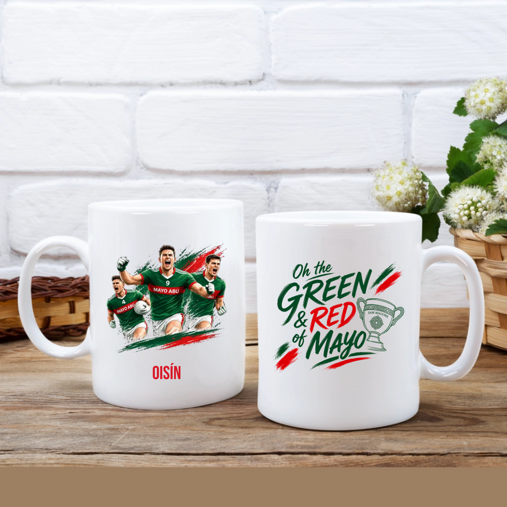 Two white ceramic mugs displayed side by side on a wooden surface in front of a white brick wall. The left mug features a graphic of football players in green jerseys with the name 'OISÍN' printed below in red.