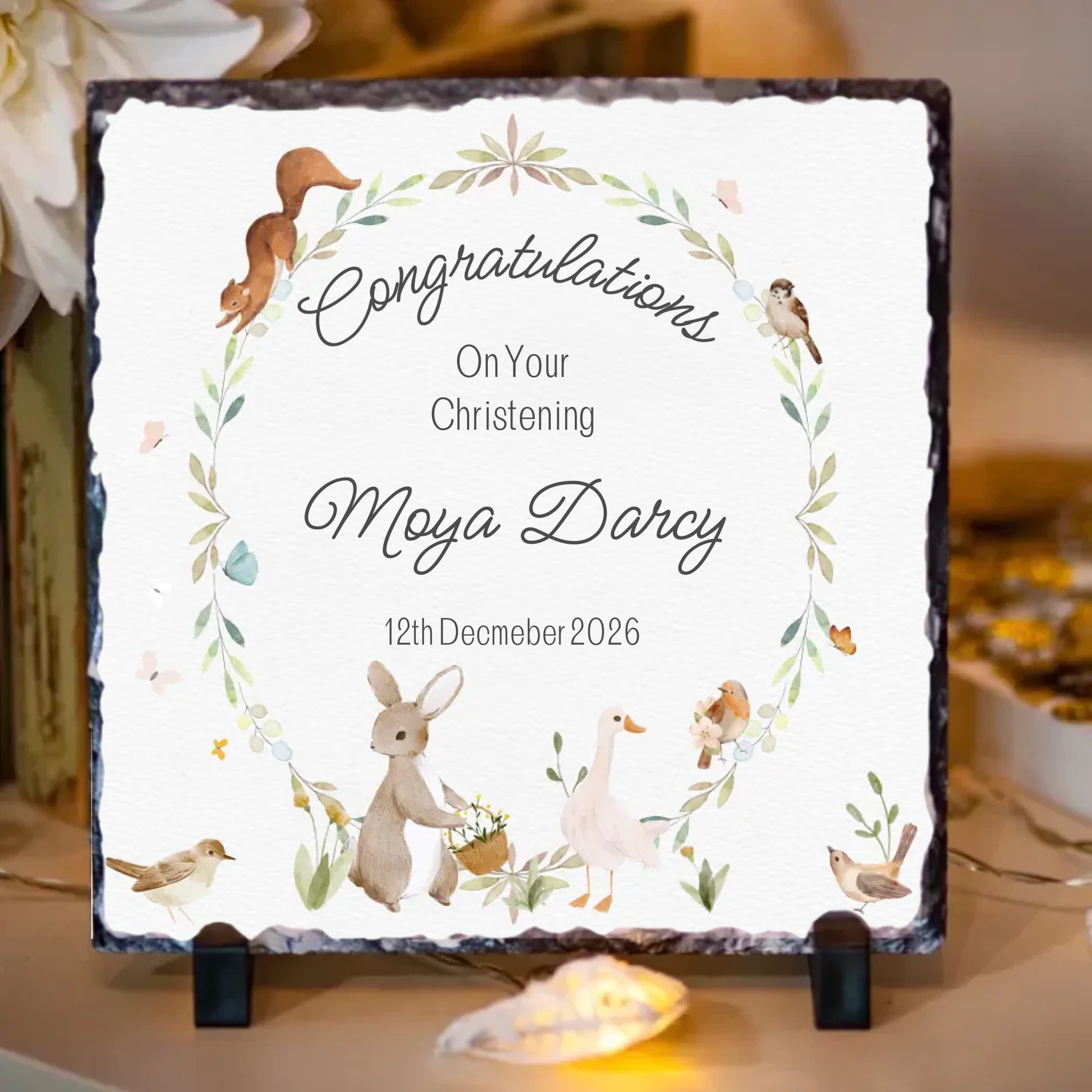 Personalized christening congratulations slate with decorative elements on a table.