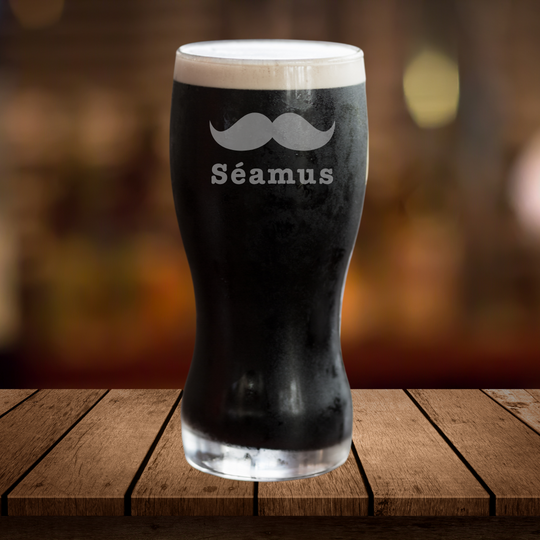 Glass of dark beer with a mustache design and 'Séamus' text on a wooden surface.