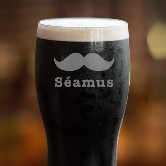 Black beer glass with a mustache design and 'Séamus' text on a blurred background