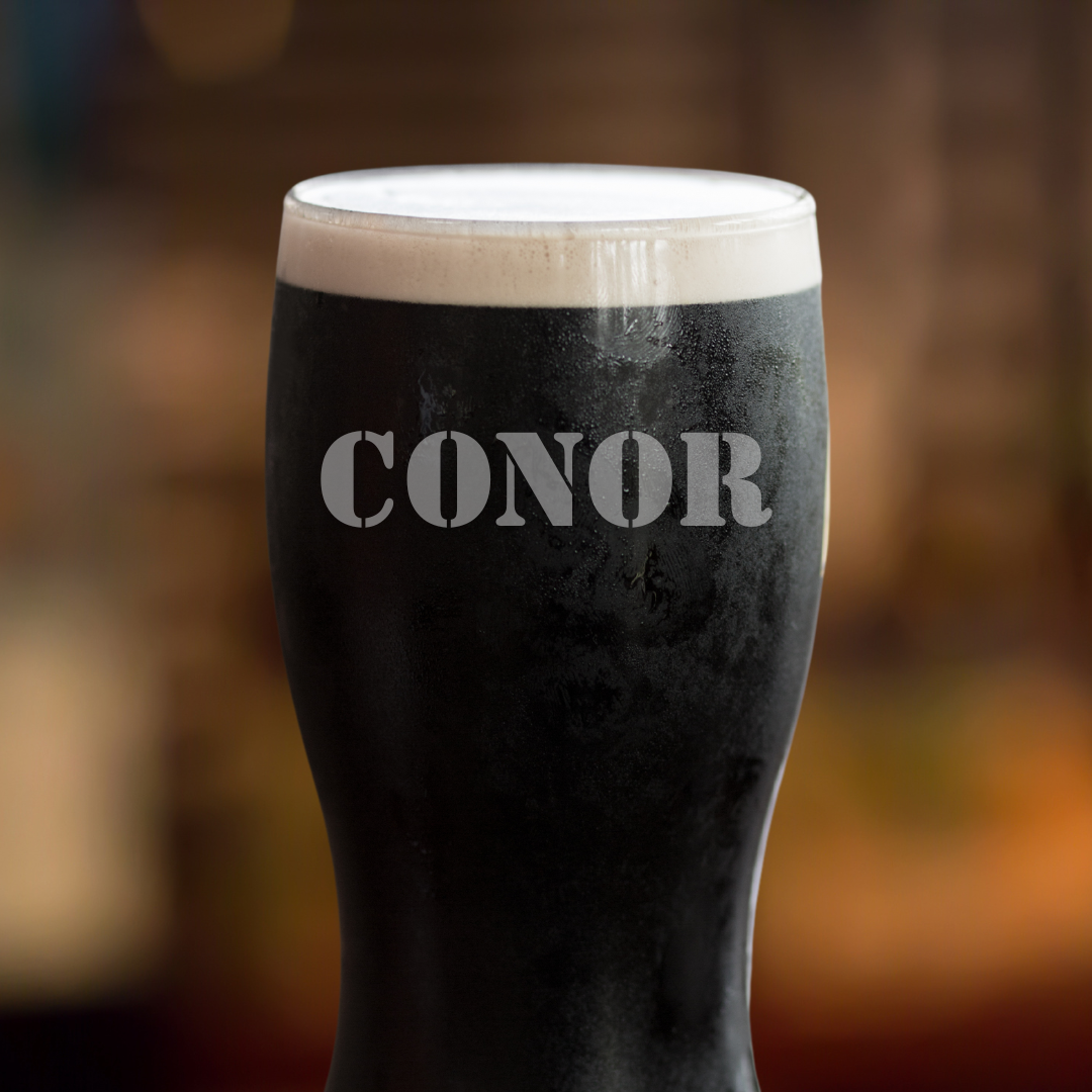 A Guinness pint glass with the name 'CONOR' etched on it, presented on a wooden surface with a blurred background.