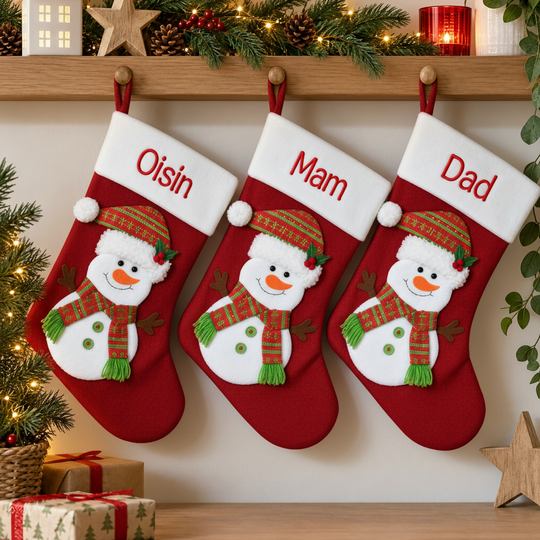Three red Christmas stockings hang on a wooden mantel decorated with greenery, candles, and wrapped gifts. Each stocking features an embroidered snowman and is personalized with the names 'Osin', 'Mam', and 'Dad' in red on white cuffs.