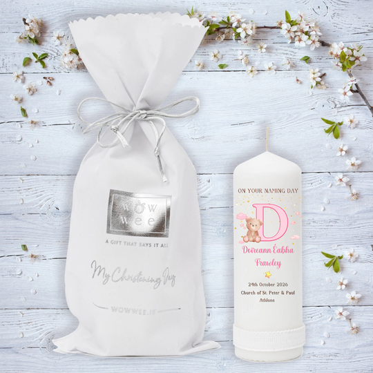 A personalized Naming Day gift set featuring a white drawstring pouch with a silver foil logo and a white candle. 
