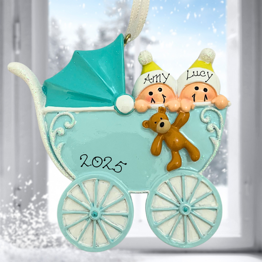 Decorative ornament of a baby carriage with two children and a teddy bear, set against a snowy window background.