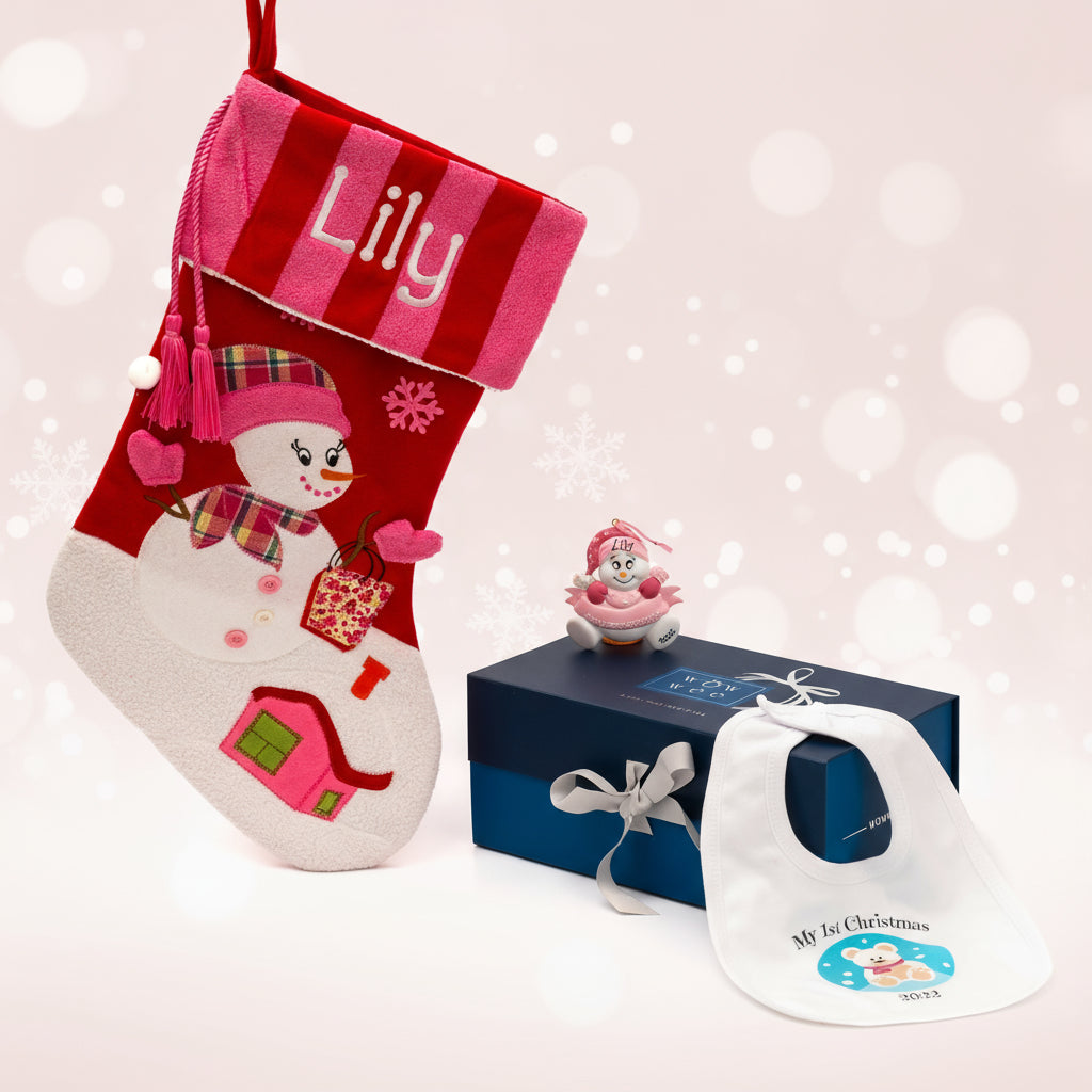 Personalised Christmas gift box for babies with a pink Christmas stocking featuring a snowman, a Christmas tree ornament, and a polar bear bib with the name 'Lily' embroidered on it, all presented in a blue and white WowWee gift box.