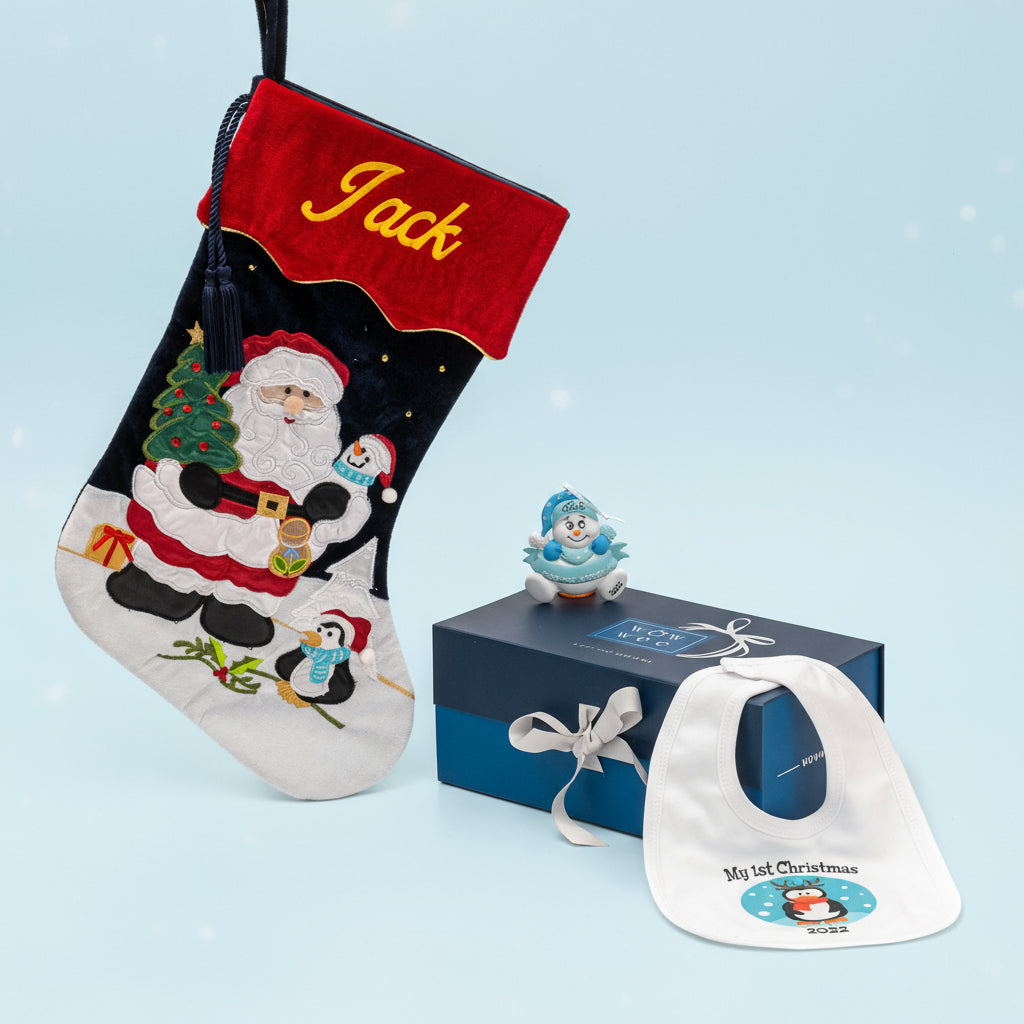 Personalized Christmas stocking in blue with the name 'Jack' embroidered, alongside a Christmas tree ornament and a penguin-themed baby bib, all presented in a blue gift box.