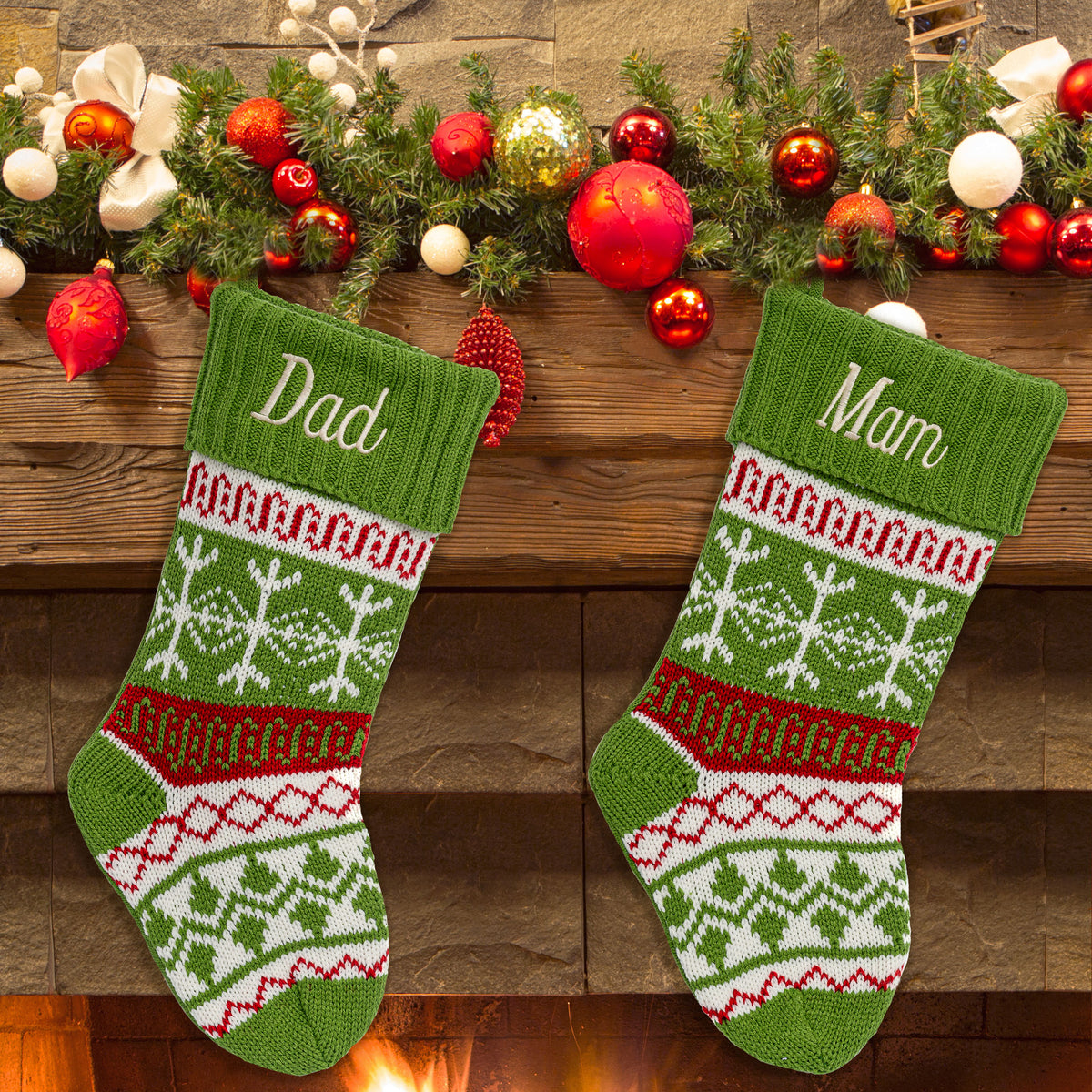 Two green Christmas stockings with snowflakes and red and white patterns, personalized with the names 'Dad' and 'Mam', displayed on a wooden mantelpiece.